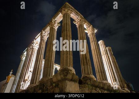 Ein dramatischer Nachtblick auf beleuchtete antike römische Tempelsäulen in Évora, Portugal, die klassische korinthische Kapitelle zeigen, verwitterte Steinruinen a Stockfoto