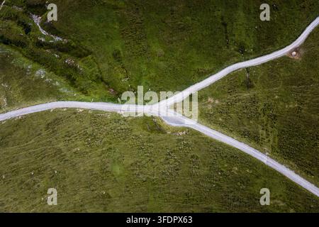 Hochwinkel-Drohnenfoto einer gabeligen Schotterstraße, die eine üppige grüne Wiese kreuzt, und zeigt ländliche Landschaftsmuster, einfache Geometrie und eine friedliche, isolierte Umgebung Stockfoto