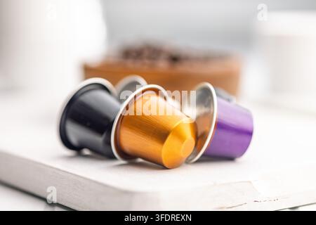 Verschiedene farbenfrohe Einzelportions-Kaffeekapseln, die auf einem hellen Tisch angeordnet sind, mit einem weichen, unscharfen Hintergrund aus Kaffeebohnen, der das morgendliche Ritual vermittelt, bequ Stockfoto