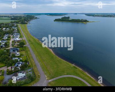 Hochwinkelige breite horizontale Luftbilddrohnenaufnahme, die einen weitläufigen Blick auf die Küstenstraße, den Grasdamm und das Wohngebiet am Wasser in der Nähe von R einfängt Stockfoto