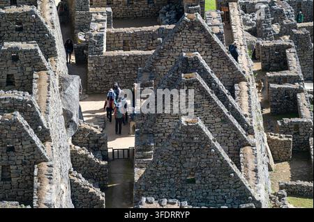 Touristen gehen schmale Pfade zwischen alten Inka-Steinbauten in Machu Picchu, Peru, und erkunden Terrassen und Korridore der historischen Zitadelle Stockfoto