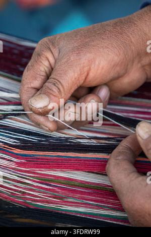 Geschickte Handwerkerhände weben helle Fäden zu einem gemusterten Textil, Nahaufnahme von Fingern, Garn und Webstuhl, die traditionelle Handwerkskunst einfangen Stockfoto