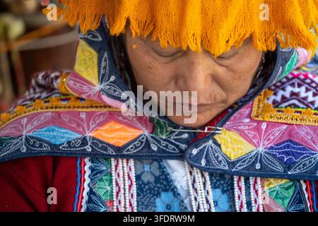 Peruanische Andenfrau, die lebhafte bestickte Textilien und einen gelben Fransenhut trägt, blickt nach unten in einem Nahaufnahmeporträt, das die Tradition hervorhebt Stockfoto