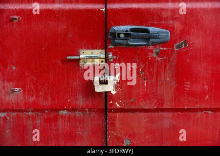 Vintage rote Lieferwagen-Hecktüren mit Metallriegel, Vorhängeschloss und rissiger Lacktextur. Nahaufnahme der verwitterten roten Hecktüren eines alten gewerblichen Lieferwagens. Stockfoto