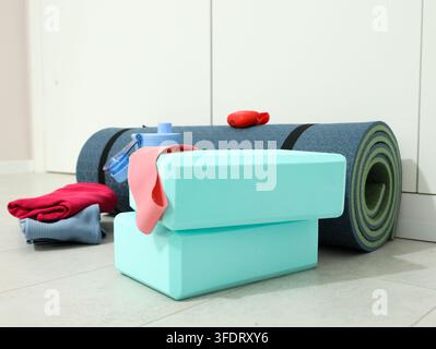 Gerollte Yogamatten, Schaumstoffblöcke, Widerstandsbänder, Wasserflasche und gefaltete Handtücher, die auf sauberem Boden in einem hellen Heimstudio angeordnet sind, zeigen organisierte Fitness Stockfoto