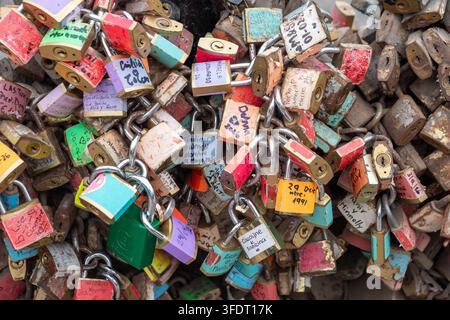 Ein dichter Cluster farbenfroher Liebesschlösser und Vorhängeschlösser, die an Metallketten auf einer Brücke befestigt sind, viele handgeschrieben mit Namen und Daten, die Romantik vermitteln Stockfoto