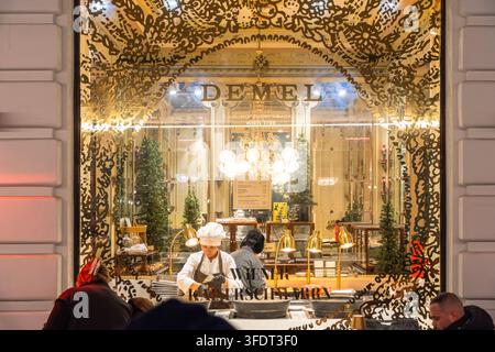 Konditoren bereiten Kaiserschmarrn hinter dem beleuchteten Schaufenster des berühmten Café Demel in Wien, Österreich, während Besucher sie beobachten, während Stockfoto