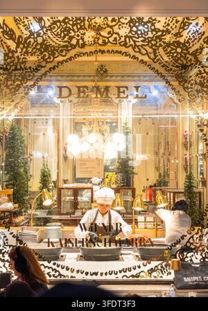 Konditoren bereiten Kaiserschmarrn hinter dem beleuchteten Schaufenster des berühmten Café Demel in Wien, Österreich, während Besucher sie beobachten, während Stockfoto