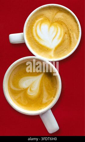 Zwei Tassen Kaffee-Cappuccino mit Herzform auf einem roten Tischtuch. Stockfoto