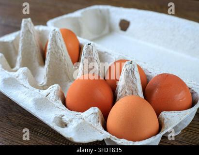 Braune Eier in einer offenen Pappschachtel aus recyceltem Papier, die auf einem Holztisch platziert ist. Nahaufnahme. Täglicher Lebensmitteleinkauf, organische Proteinquellen und kulinarische Zutaten Stockfoto