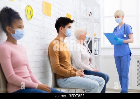 Coronavirus-Behandlung. Verschiedene Menschen sitzen in der Schlange und warten auf den Arzttermin, Krankenschwester spricht mit Patienten im Wartezimmer des Krankenhauses. Covid-1 Stockfoto