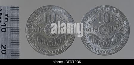 Zwei Münzen aus der Zeit des Ersten Weltkriegs aus Düren, Deutschland, datiert auf 1917, mit erhabener Schrift und einem zentralen Blumenmotiv, ausgelegt neben einem Lineal zur Größenvergleich. Stockfoto