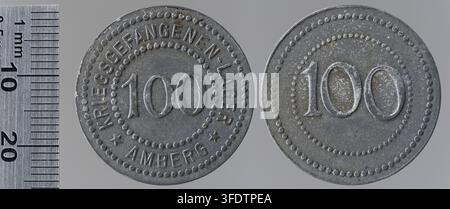 Zwei Metallmarken aus der Zeit des Ersten Weltkriegs, jeweils mit der Markierung „100“ und zusätzlichem Text, aus Amberg, Deutschland, fotografiert neben einem Millimetermaßstab, ausgegeben als Kriegsmünzen vom Kriegsgefangenenlager Amberg. Stockfoto