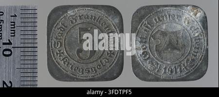 Zwei Metallmünzen aus der Zeit des Ersten Weltkriegs aus Frankenthal, Deutschland, eine 5-Pfennig-Münze mit einer zentralen Zahl und eine Münze mit einem Schild mit einem Kreuz, ausgestellt neben einem Metalllineal, Teil einer Sammlung von Kriegsmünzen. Stockfoto