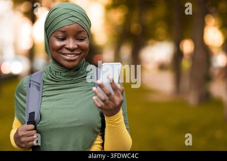 Schwarze Muslimische Studentin In Hijab Mit Smartphone Im Freien, Genießen Moderne Technologien Stockfoto