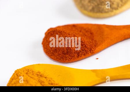 Rotes Chilipulver und Kurkuma-Gewürz auf Holzlöffeln aufgehäuft vor weißem Hintergrund Stockfoto