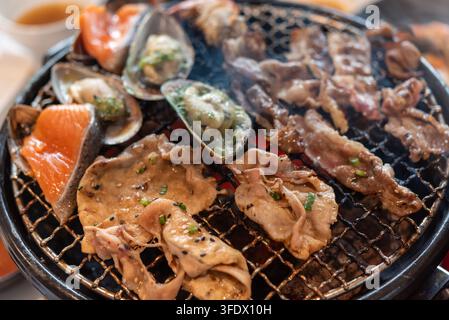 Gemischtes Fleisch, Lachs und Muscheln, die auf einem heißen Tischgrill mit herzhaften Gewürzen und Rauch für ein köstliches asiatisches Esserlebnis garen Stockfoto