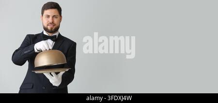 Gastgewerbe und Luxusdienstleistung, professioneller Kellner im Smoking hält silbernes Cloche-Tray mit Kopiraum für Gourmet-Presentations auf grauem Hintergrund Stockfoto