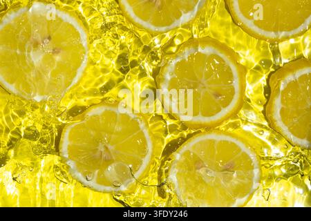 Frische Zitronenscheiben spritzen vor hellem Wasserhintergrund Stockfoto