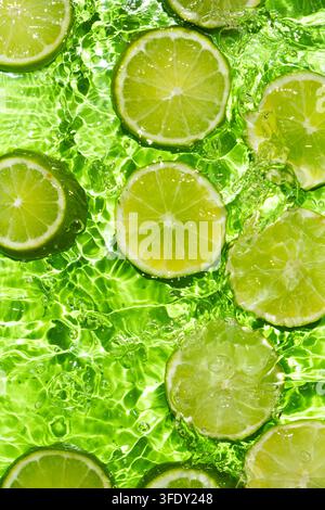 Oberblick auf frische grüne Limettenstücke, die in klarem, welligem Wasser schwimmen Stockfoto
