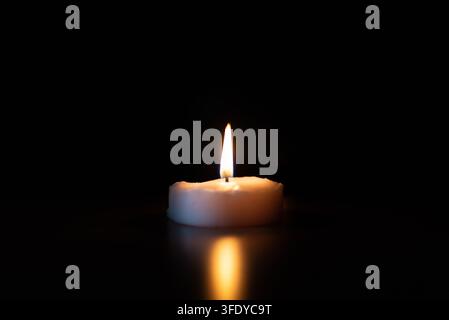 Einzige brennende Teelichtkerze im tiefen, dunklen, stillen religiösen Konzept mit großem Kopierraum. Stockfoto