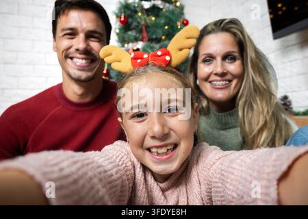 Lächelnde Tochter macht ein lustiges Selfie mit ihren Eltern, während sie zu Hause Weihnachten feiern. Stockfoto