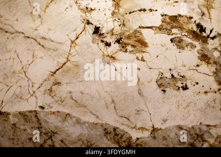 Cremige Steinstruktur mit braunen Mineralverläufen. Nahaufnahme von cremefarbenem Naturstein mit braunen Adern und kristallinen Mineralmustern. Stockfoto