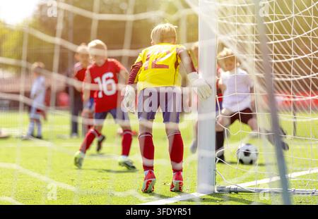 Blick durch das Tornetz von Junior-Fußballspielern, die im Bereich des Torraums angreifen und verteidigen – Jugendfußballspielaktion auf Rasenplatz Stockfoto