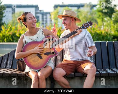 Sorgloses Paar, das durch Akustikmusik verbunden ist, während es draußen Qualitätszeit miteinander verbringt Stockfoto