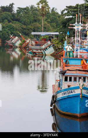 Traditionelles thailändisches Holzfischboot auf dem Tha Phae Kanal, mit versunkenen Anglerbooten im Hintergrund, Nakhon Si Thammarat, Thailand. Nur für redaktionelle Nutzung. Stockfoto