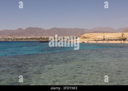 Klares türkisfarbenes Wasser über einem flachen Korallenriff in der Nähe des Movenpick Resorts Sharm El Sheikh, Ägypten, mit der Küste des Roten Meeres in der Ferne Stockfoto