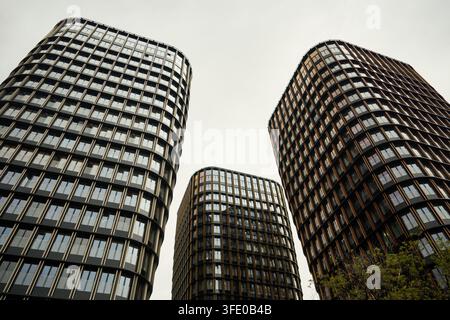 Geschwungene moderne Bürotürme mit sich wiederholender Glasfassade, die sich gegen den blassen Himmel erheben, mit Architektur, Gebäude, Wolkenkratzer, Bürodetail, das Turm zeigt Stockfoto