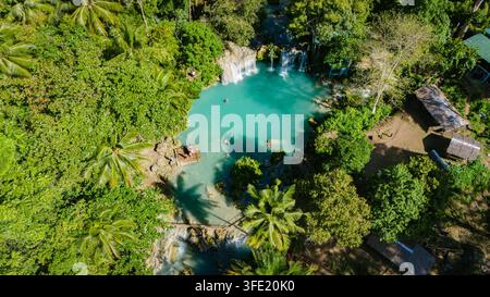 Luftaufnahme der Cambugahay-Wasserfälle mit türkisfarbenem Wasser, üppigem tropischen Wald und Menschen auf einem Bambusfloß in Siquijor, Zentralvisayas, Philippinen. Stockfoto
