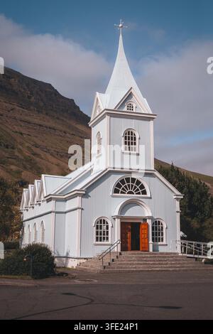 Seyðisfjarðarkirkja, die Blaue Kirche, in Seyðisfjörður Island, unter den umliegenden Berghängen, August 2026 Stockfoto