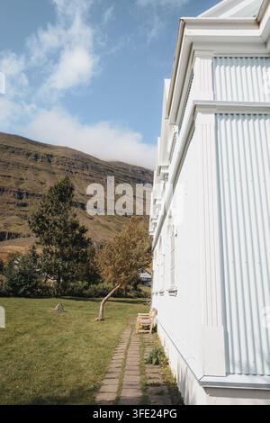 Seyðisfjarðarkirkja, die Blaue Kirche, in Seyðisfjörður Island, unter den umliegenden Berghängen, August 2026 Stockfoto