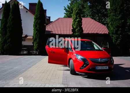 Kiew, Ukraine - 29. Juli 2026: Ein hellroter Opel Zafira-Kombi mit offenen Türen, der auf einer gepflasterten Einfahrt neben einem Haus unter klarem Himmel geparkt ist. Stockfoto