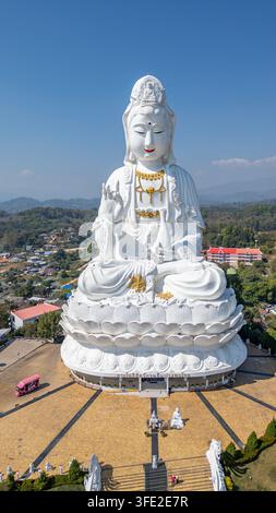 Vertikale Aufnahme, die die massive weiße Guan-Yin-Statue zeigt, die auf einem Lotus-Sockel über dem Hauptplatz und den Treppen von Wat Huay Pla Kang in Thailand sitzt. Stockfoto