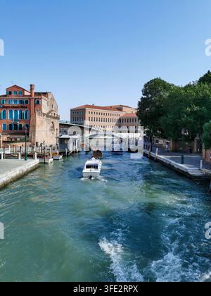 Blick auf einen Kanal in Venedig mit traditionellen Booten, die zwischen historischen venezianischen Gebäuden unter einem klaren blauen Himmel an einem hellen Sonnentag in Italien festgemacht sind. Stockfoto