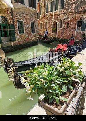 Blick auf einen Kanal in Venedig mit traditionellen Booten, die zwischen historischen venezianischen Gebäuden unter einem klaren blauen Himmel an einem hellen Sonnentag in Italien festgemacht sind. Stockfoto