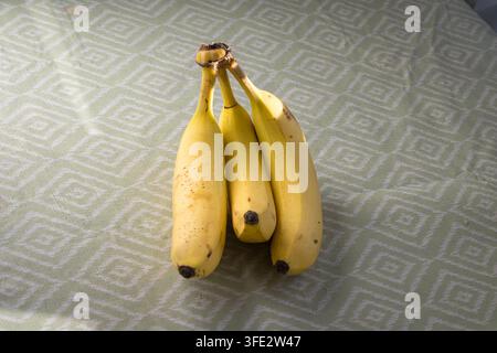 Ein Büschel reifer Bananen ruht auf einem geometrisch gemusterten Tischläufer und fängt die Essenz von gesunder Ernährung und natürlicher Frische ein. Ideal für die Verwendung in f Stockfoto