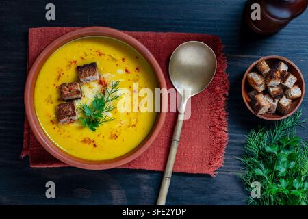 Cremige Kürbis- oder Karottensuppe mit Croutons und Kräutern, Blick von oben, Nahaufnahme. Köstliche gelbe Gemüsepüreesuppe in einer Keramikschale, serviert mit knusprigem Stockfoto