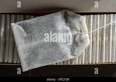 Einzelne Papier-Teebag oben auf einer organisierten Reihe in der Schachtel. Nahaufnahme von oben der klassischen weißen Teebag mit Faden, die horizontal über einer ordentlichen Reihe der Packung liegt Stockfoto