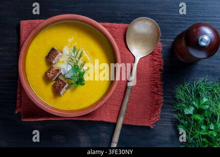 Kürbiskremesuppe mit Croutons und Kräutern, Nahaufnahme. Cremige gelbe Gemüsesuppe mit Croutons, Käse und frischen Kräutern in der Schüssel. Rustikales Flat-Lay-Essen Stockfoto