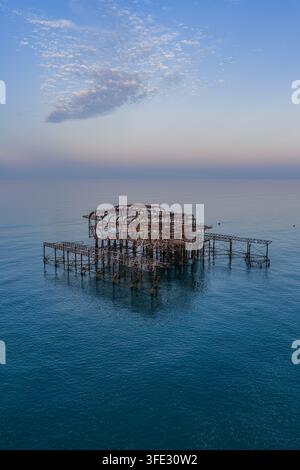 Luftaufnahme der Skelettreste des historischen West Piers, der bei Sonnenuntergang mit einem klaren blauen Himmel in der ruhigen See in Brighton und Hove, England, steht Stockfoto