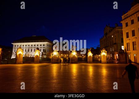 Beleuchtetes Matthiastor und Eingang zur Prager Burg bei Nacht, mit Besuchern, die den ersten Hof überqueren. Stockfoto