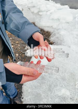 Eine Nahaufnahme eines Touristen oder Abenteurers in einer blauen Jacke, der lange, durchsichtige Eiskristalle in den Händen hält Stockfoto