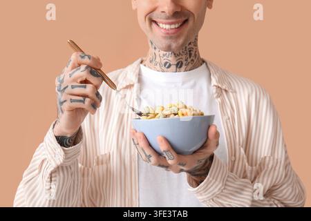 Mann hält Schüssel mit Müsliringen und Löffel auf beigefarbenem Hintergrund Stockfoto