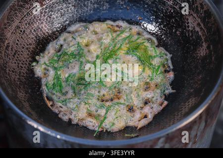 Cha om Acacia-Blatt-Omelett in heißem Öl in einem Wabenstahl-Wok in Thailand braten, Ansicht von oben auf lokales Straßenessen. Stockfoto