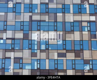 Wiederholendes Raster aus blauen Fenstern und rechteckigen Fassadenplatten erzeugt ein geometrisches Muster an einem modernen Hochhaus. Stockfoto