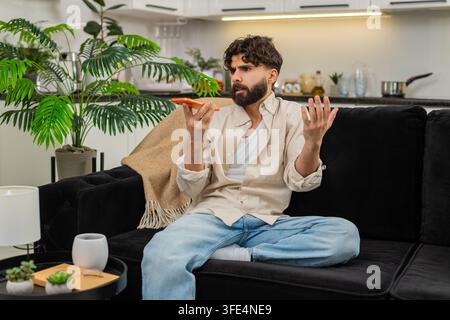 Indischer Mann zu Hause verwendet Smartphone-Lautsprecher Streiten mit Bank-Support über Betrug Anruf fühlt sich wütend. Arabian Guy ruft oranges Handy wegen Spam-Problemen mit Kartengebühren an und fühlt sich frustriert. Stockfoto